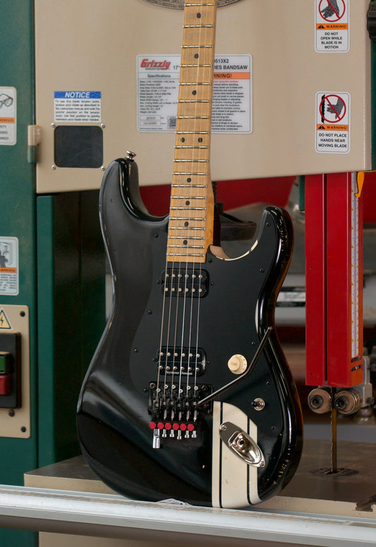Black electric guitar on a workbench with a red wall and another guitar in the background