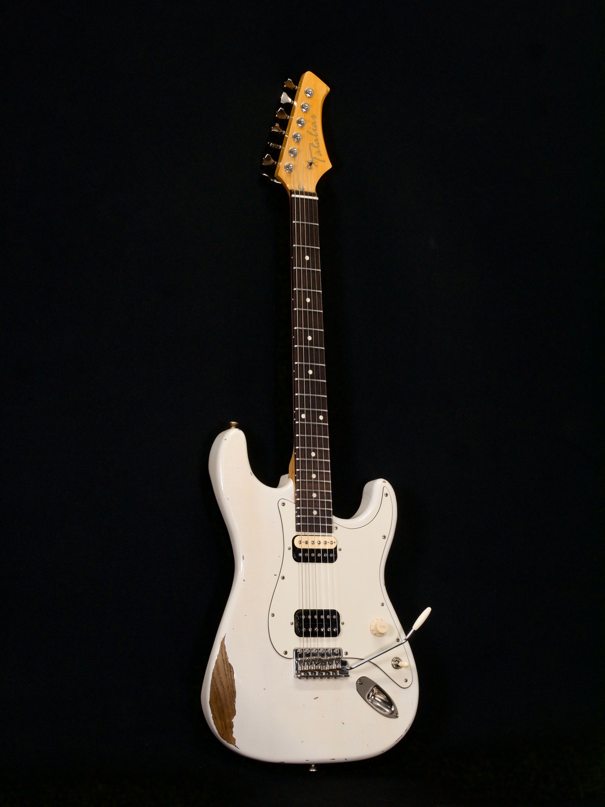 White electric guitar with a pickguard on a black background