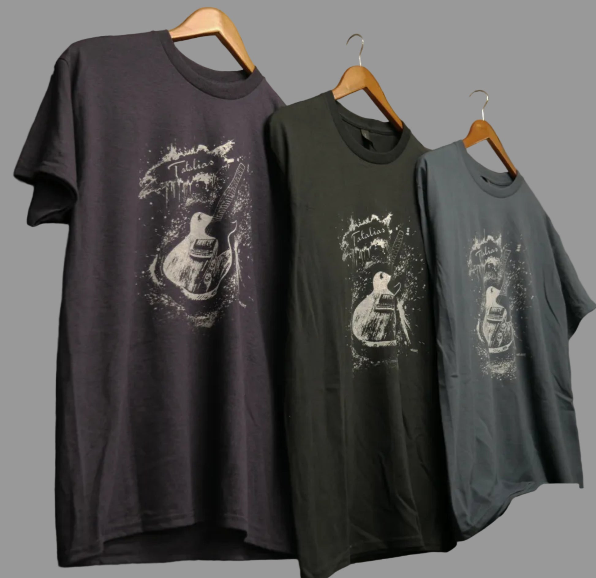T-shirts with guitar designs hanging on a wall next to guitars